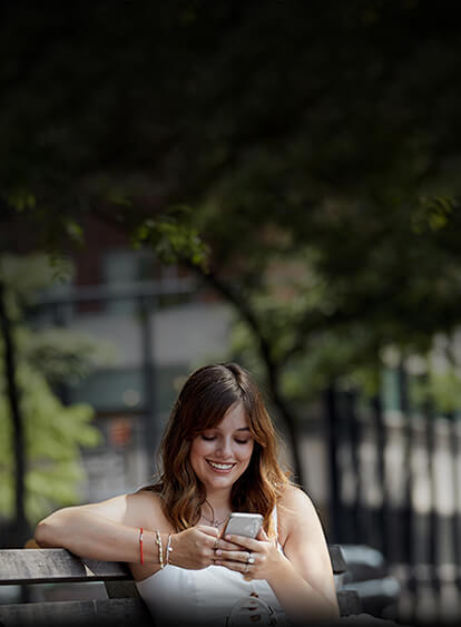 Young woman enjoying her 5G phone outside on park bench.