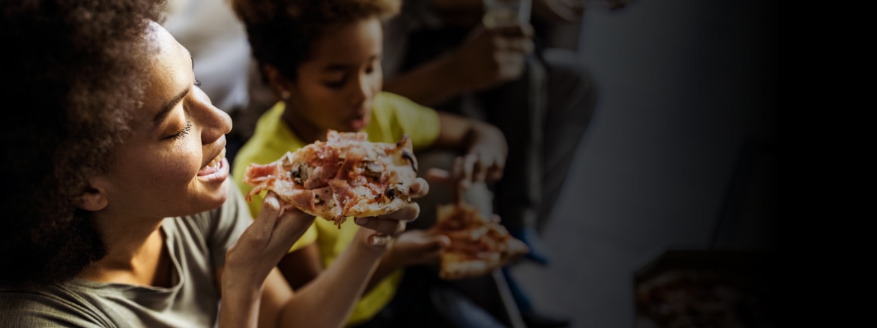 Woman and child smiling while eating pizza.